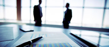 Business document with pen, two blurred figures in background.