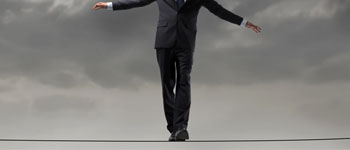 Businessman in suit balancing on a tightrope under cloudy sky.