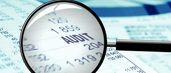 Magnifying glass focusing on the word 'audit' in financial documents.